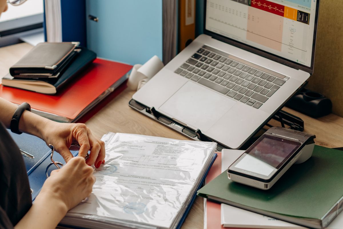 Financial records being organized in binders beside a laptop
